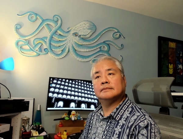 Me in my office, as seen from the point of view of my webcam. In the background is a large painting of an octopus, a computer screen showing a “Space Invaders” desktop background, and my collection of rubber ducks.