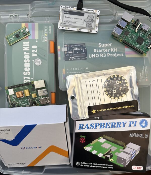 Joey de Villa’s “IoT box” — a clear plastic storage container containing Pimoroni Badger 2040W, Elegoo UNO R3 Super Starter Kit, Rasberry Pi 3 Model B, Adafruit Circuit Playground Express, 2 Raspberry Pi 4 Model Bs, Elecrow 5" HDMI screen, Elegoo 37 sensor module kit, and Raspberry Pi Pico.